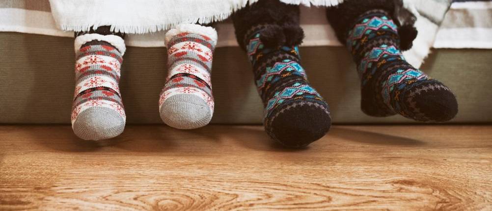 Kuschelsocken-Test: Ein großes und ein kleineres Paar Füße mit Kuschelsocken schauen unter einer weißen Decke hervor.