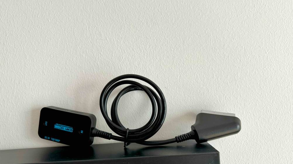 Getestet: Ein Scart-HDMI-Konverter liegt auf einer dunkeln Fläche vor einer hellen Wand.