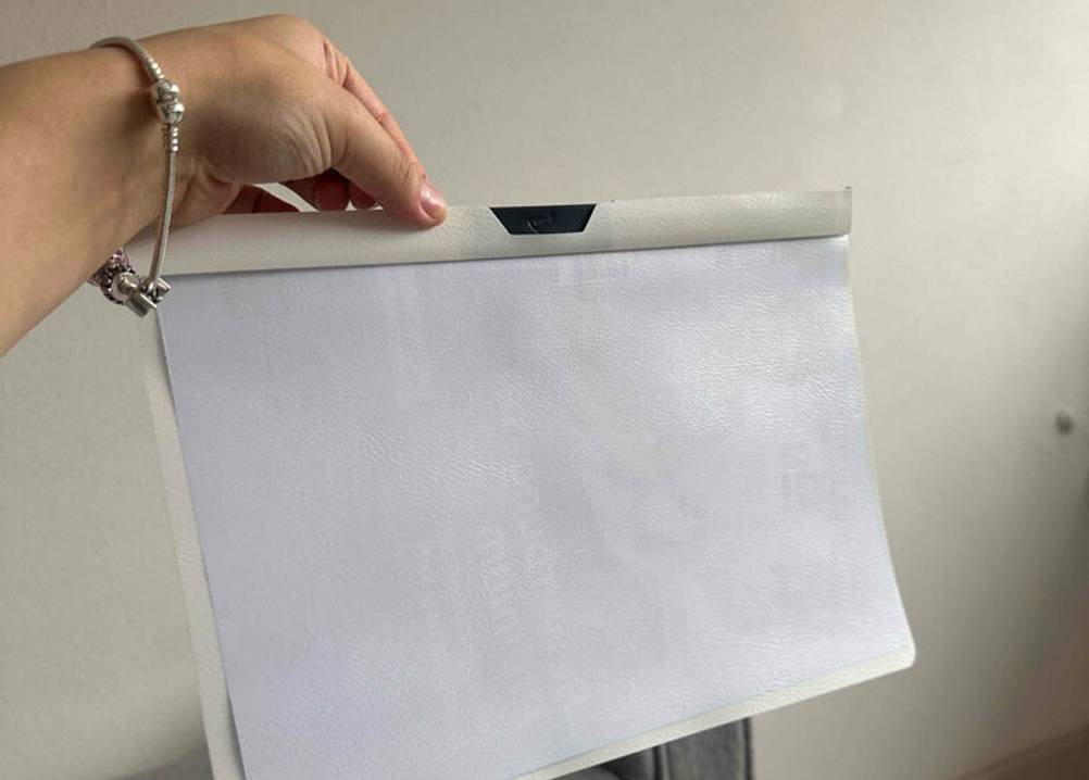 Eine Damenhand hält eine weiße, getestete Bewerbungsmappe an der Klemmvorrichtung, die für einen Halt der Blätter sorgt.