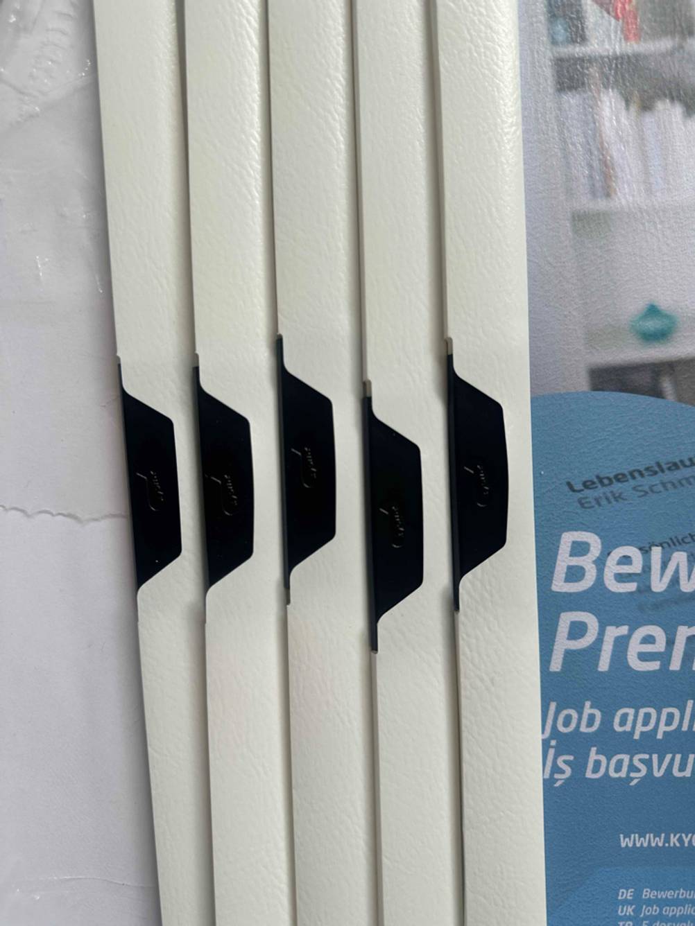 Getestet: Bewerbungsmappen aus weißem Kunststoff, mit Fokus auf die schwarzen, schwenkbaren Klemmen.