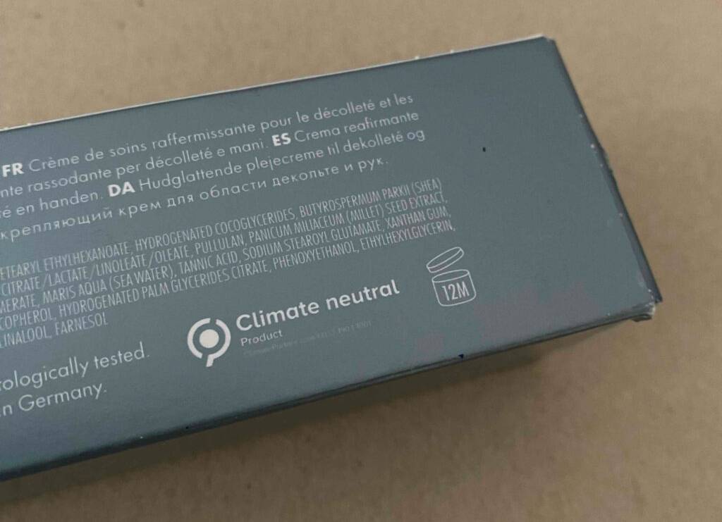 Eine graue, klimaneutral hergestellte Verpackung der Dekolleté-Creme im Test liegt auf einem braunen Untergrund.