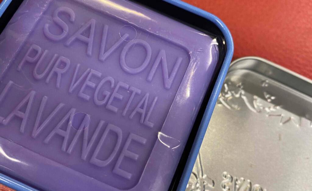 Eine vegane, violettfarbene Duschseife im Test befindet sich innerhalb ihrer Box auf einer roten Oberfläche.