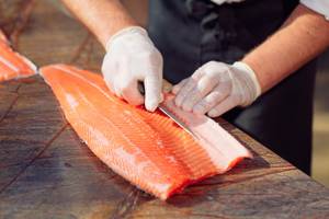 Lachsmesser-Test: Koch mit weißen Handschuhen filetiert Lachs.