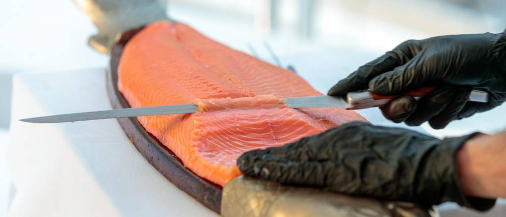 Lachsmesser-Test: zwei Hände in schwarzen Handschuhen filetieren Lachs.
