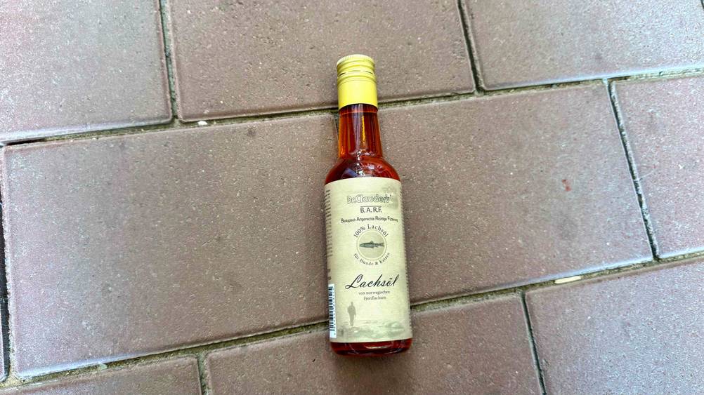 Auf einem Steinboden liegt eine Flasche des getesteten Lachsöl Katze.