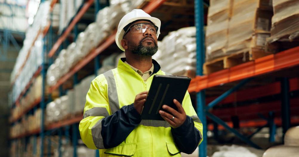 Ein Mann steht mit einem Tablet in einem Lager und sucht Waren.