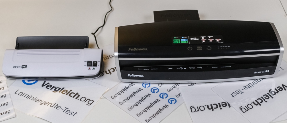 Ein weißes A4-Laminiergerät und ein schwarzes A3-Laminiergerät stehen auf einem weißen Tisch.