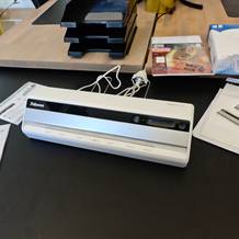 Das Laminiergerät Fellowes Saturn 3i steht auf einem schwarzen Schreibtisch.