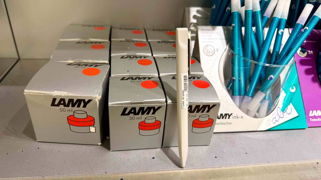 Im Test: Ein weißer Lamy-Kugelschreiber steht angelehnt an mehrere Lamykartons in einem Regal.