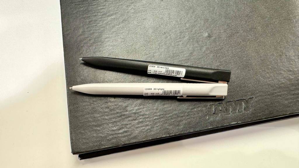 Zwei Lamy-Kugelschreiber, einer schwarz, einer weiß, liegen zum testen auf einer schwarzen Lamy-Lederfläche.