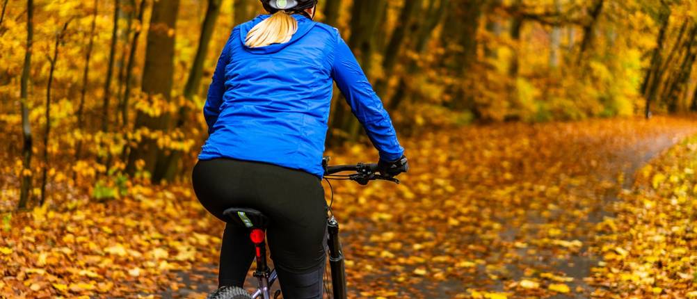 Fahrradhose-Unisex-Test: Radfahrerin in langer Fahrradhose fährt durch einen herbstlichen Wald.