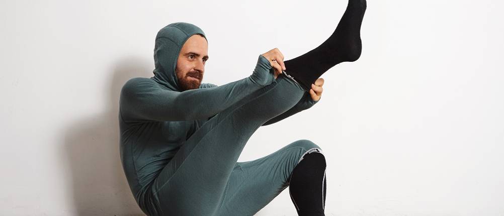 Lange-Unterhose-Herren-Test: Ein Mann in langer Unterhose und Overall zieht sich Socken an.