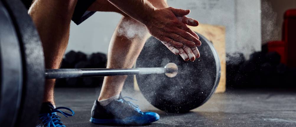 Langhanteln im Test: Mann hockt neben einer Langhantel und reibt die Hände mit Magnesium ein.