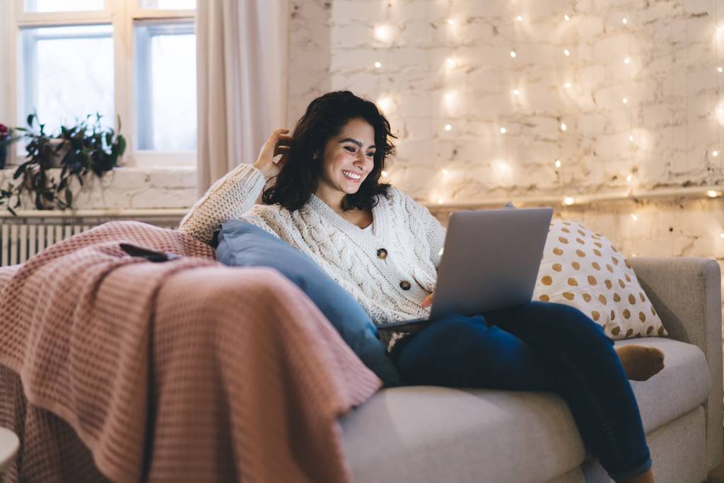 Eine Frau mit Laptop auf dem Sofa sitzend.