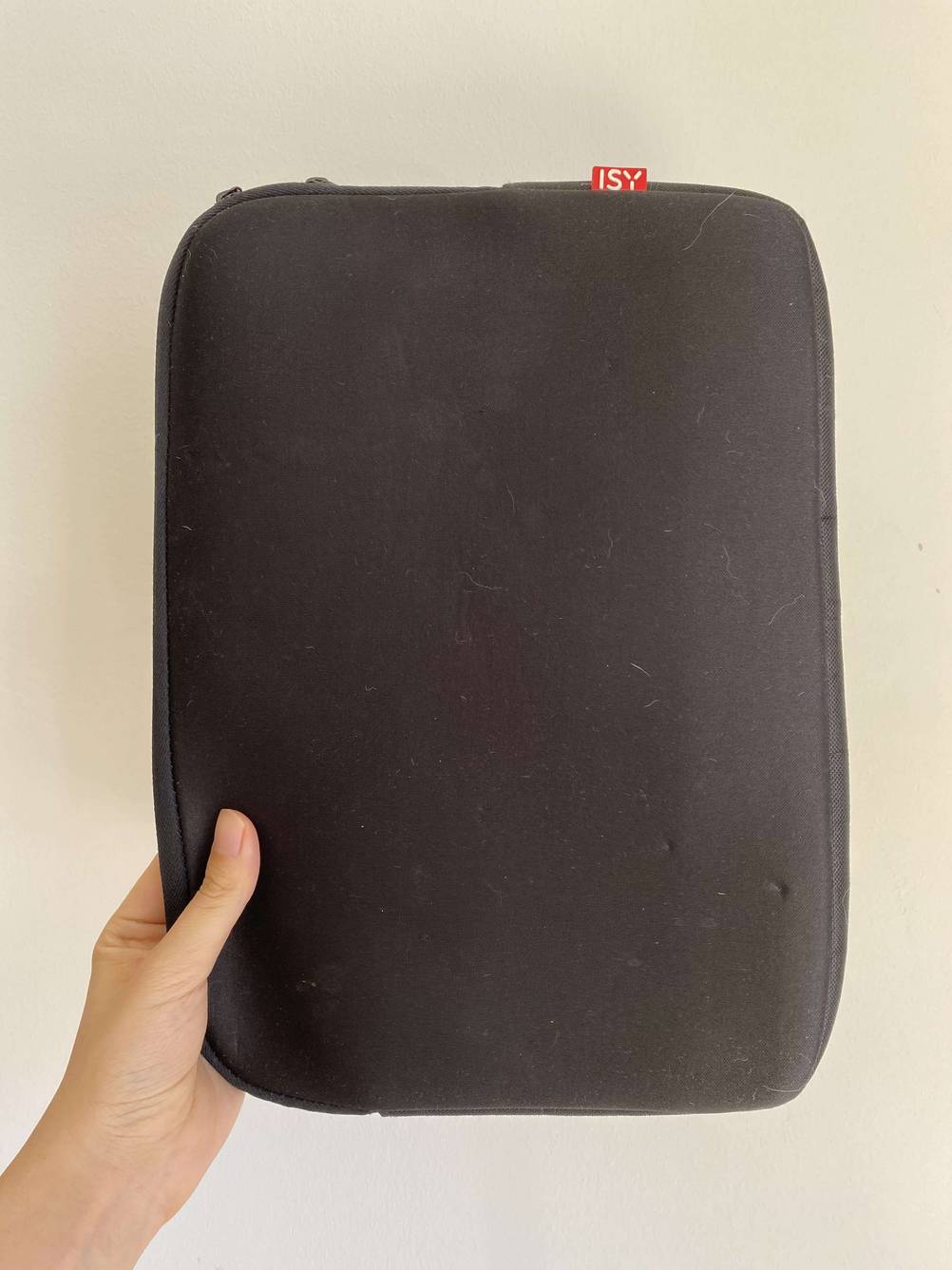 Eine Hand hält ein getestetes Laptop-Sleeve vor eine helle Wand.