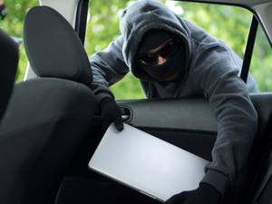 Laptop-Versicherung-Test: Ein maskierter Mann stiehlt einen Laptop aus einem Auto.