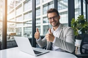 Laptop-Versicherung-Test: Ein Mann sitzt lächelnd vor seinem Laptop und zeigt mit beiden Daumen nach oben.