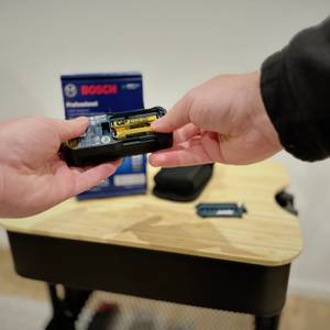 Eine Person öffnet das Fach der Batterien des Laser-Entfernungsmessers von Bosch.