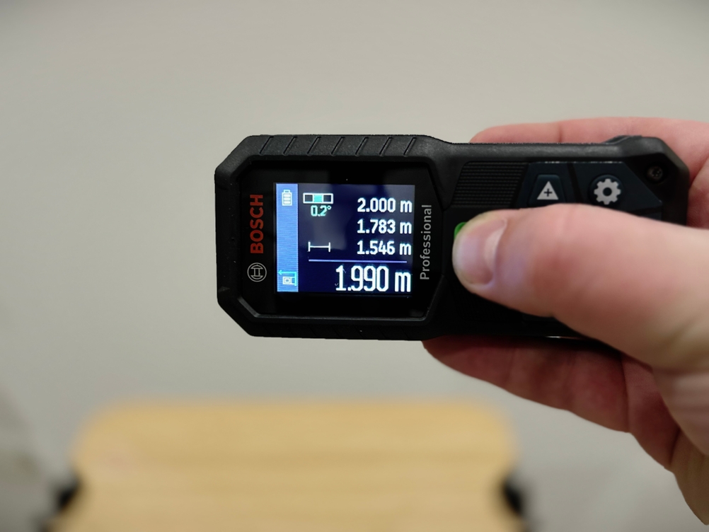 Eine Hand bedient den Laser-Entfernungsmesser von Bosch in waagerechter Position.