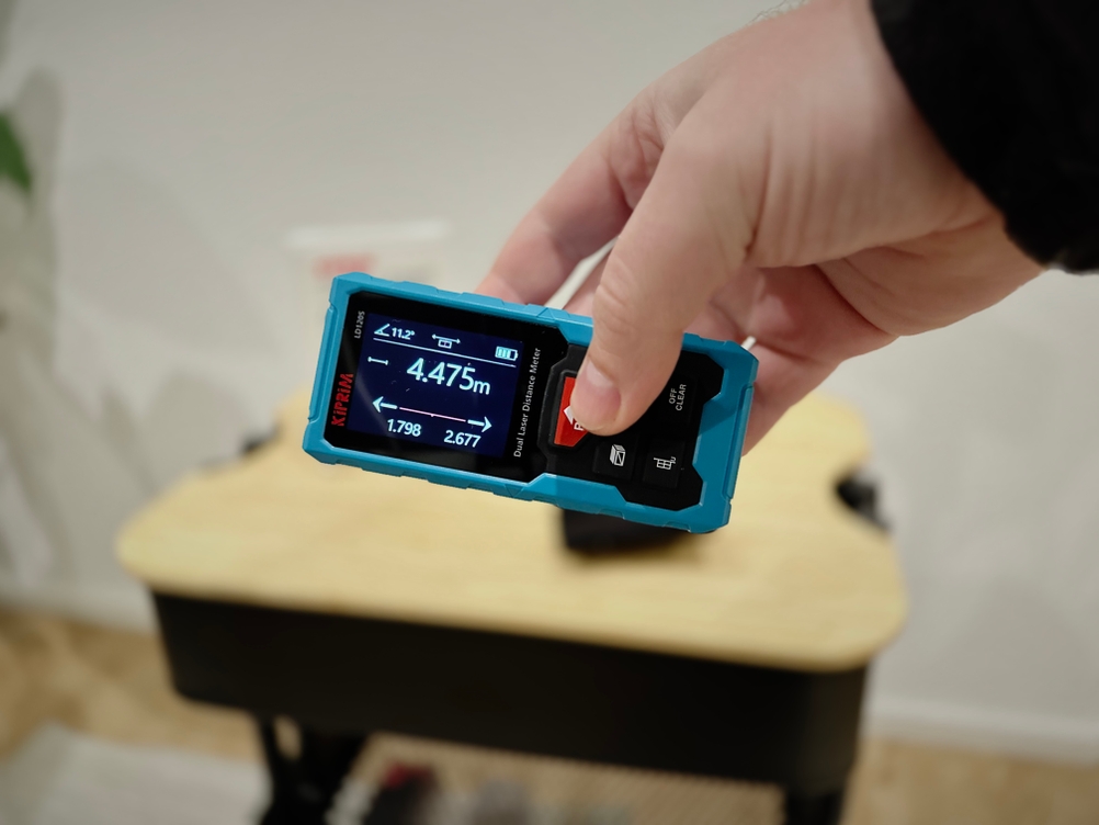 Eine Hand hält den Kiprim-Laser-Entfernungsmesser schräg waagerecht.