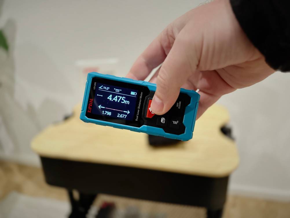 Eine Hand hält den Kiprim-Laser-Entfernungsmesser schräg waagerecht.