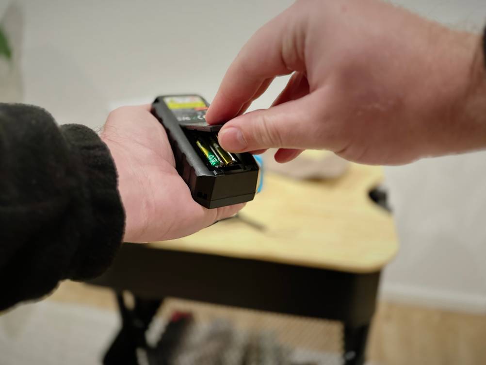 Zwei Hände halten den Mileseey-Laser-Entfernungsmesser und öffnen das Batteriefach.