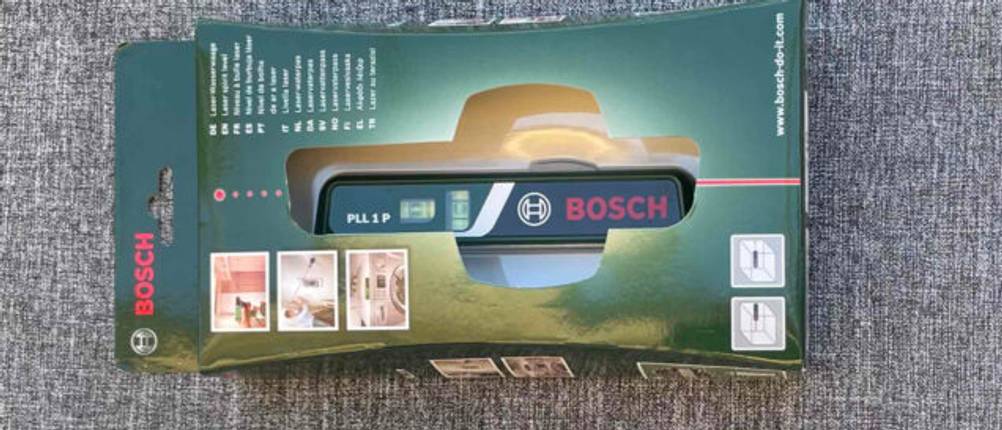 Die Originalverpackung einer getesteten Laser-Wasserwaage mit Sichtfenster auf einer grauen Fläche.
