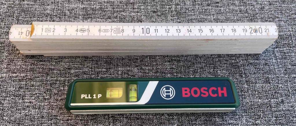 Die getestete Laser-Wasserwaage liegt neben einem Zollstock.