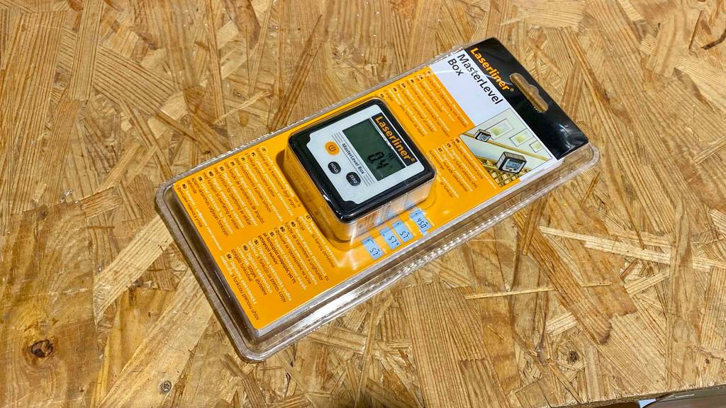 Blick von oben auf eine original verpackte digitale Wasserwaage, die zum testen auf einer Spanholzplatte liegt.
