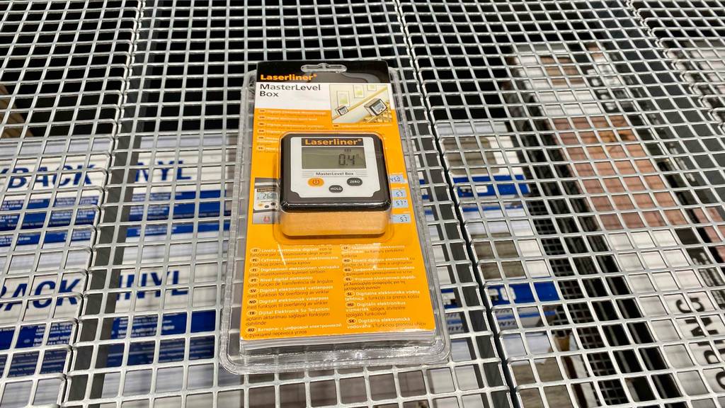 Im Test: Eine digitale Wasserwaage liegt in Originalverpackung auf einem Lochregal, unter dem Kartons stehen.