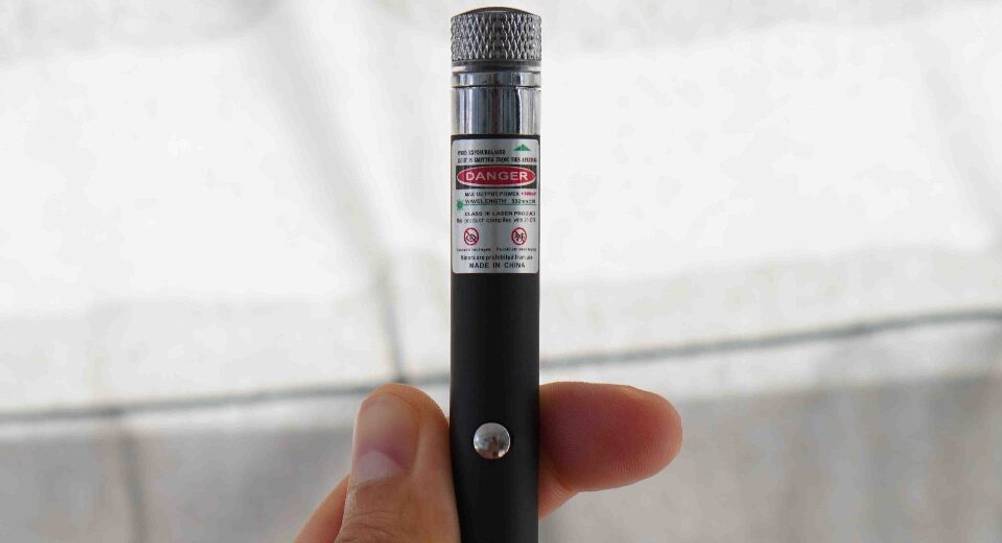 Detailansicht des Etiketts inklusive Warnhinweise eines getesteten Laserpointer-Stifts in einer Hand vor hellgrauem Hintergrund.