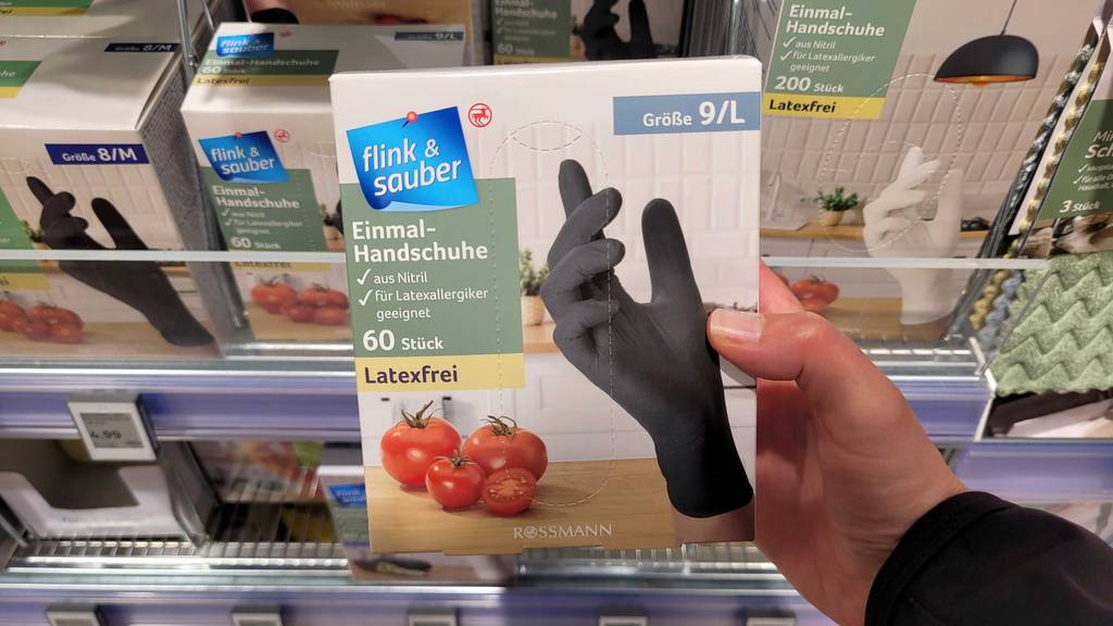 Eine Hand hält eine Packung mit den Größe-L-Einmalhandschuhen im Test vor einem Regal.