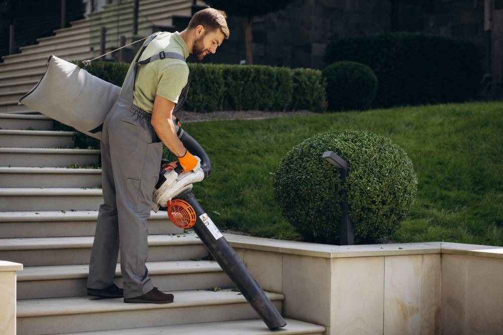 Ein Arbeiter mit Laubsauger saugt eine Treppe frei.