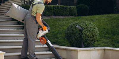 Ein Arbeiter mit Laubsauger saugt eine Treppe frei.