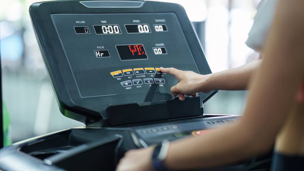 Das Display eines getesteten Laufbands mit Steigung in Nahaufnahme. Eine Frau tippt mit dem Finger auf einen Button.