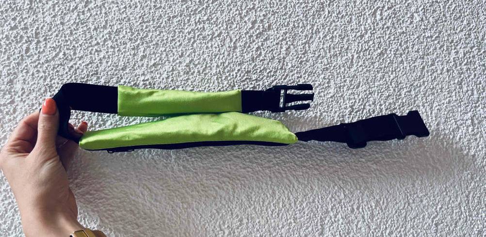 Hand hält einen getesteten Stretch Laufgürtel vor weißer Wand.