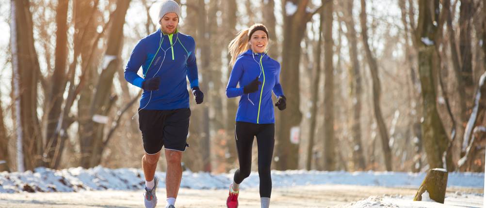 Laufhandschuhe-Test: Ein Mann und eine Frau laufen in einer winterlichen Landschaft. Beide Läufer tragen Laufhandschuhe. 