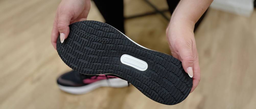 Jemand hält den Adidas Damen-Laufschuh in der Hand, sodass die Sohle von unten zu sehen ist.