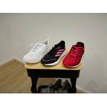 Jeweils ein Damen-Laufschuh aller drei getesteten Marken, also Adidas, Puma und Whitin, stehen aufgereiht nebeneinander auf einem Rollwagen.