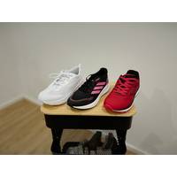 Jeweils ein Damen-Laufschuh aller drei getesteten Marken, also Adidas, Puma und Whitin, stehen aufgereiht nebeneinander auf einem Rollwagen.