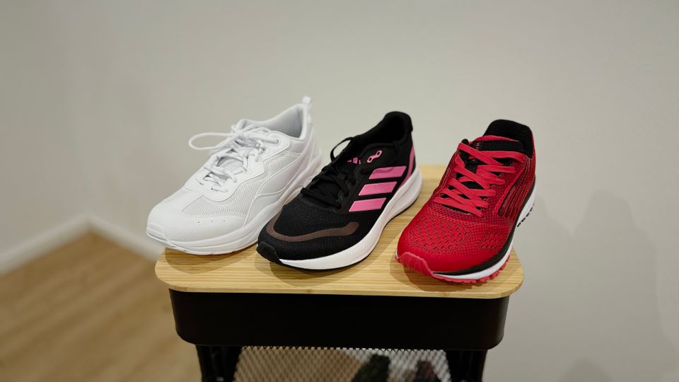 Jeweils ein Damen-Laufschuh aller drei getesteten Marken, also Adidas, Puma und Whitin, stehen aufgereiht nebeneinander auf einem Rollwagen.