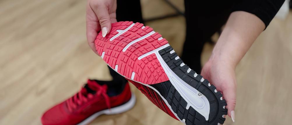 Jemand hält den Whitin Damen-Laufschuh in der Hand, sodass die Sohle von unten zu sehen ist.