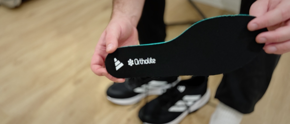 Eine Person hält eine schwarze Ortholite-Einlegesohle mit aufgedrucktem Adidas-Logo in der Hand.
