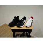 Auf einem Holzschemel liegt jeweils der linke Laufschuh jeder Marke dieses Vergleiches. Auf dem Bild sieht man von links den schwarzen Feethit, in der Mitte den schwarzen Adidas und rechts den weißen Puma.