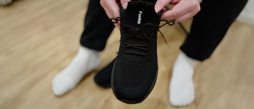 Eine Person hält mit beiden Händen einen Feethit Sneaker Laufschuh und zeigt die Form des Schuhs.