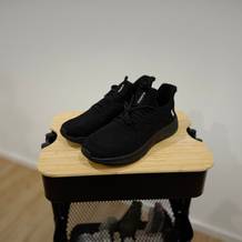 Schwarze Feethit Sneaker Laufschuhe stehen auf einem Holzhocker.