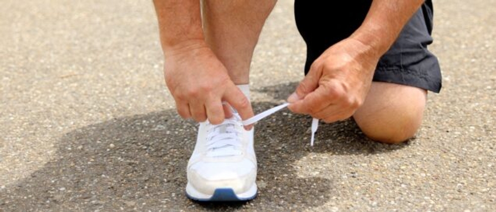 Ein Mann kniet sich nieder, um die Schnürsenkel eines Laufschuhs zu binden.