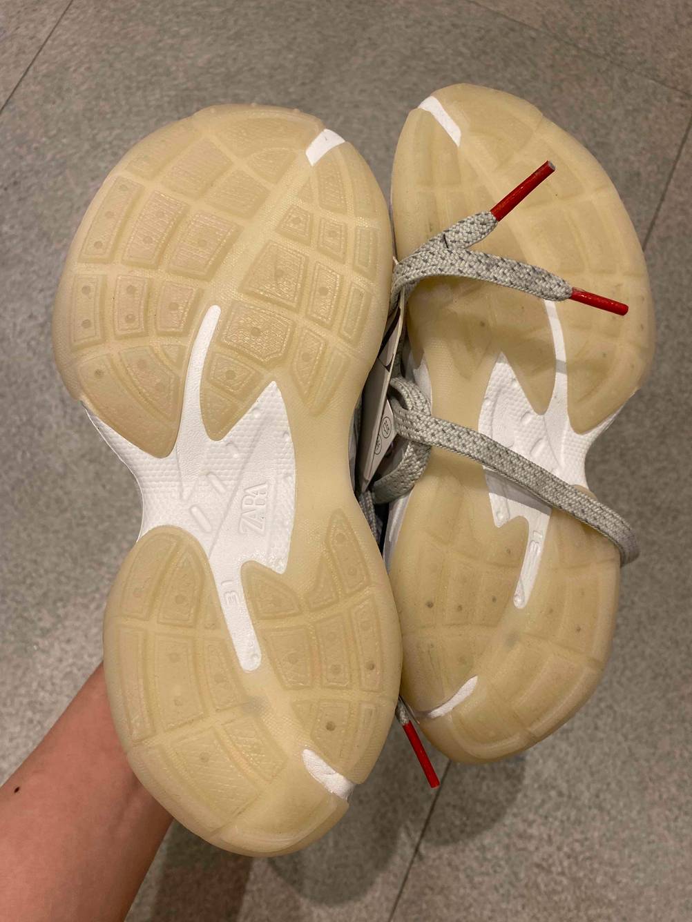 Im Test: Sohlen der Laufschuhe für Kinder von einer Hand vor einen grauen Boden gehalten.