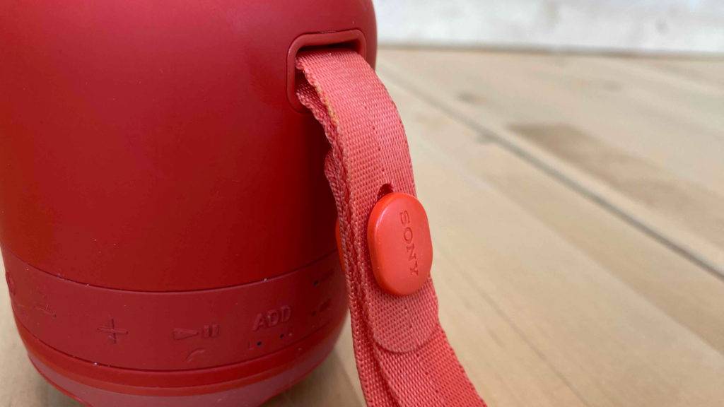 Lautsprecher von Sony steht auf einem Laminatboden und zeigt die Trageschlaufe vorne.