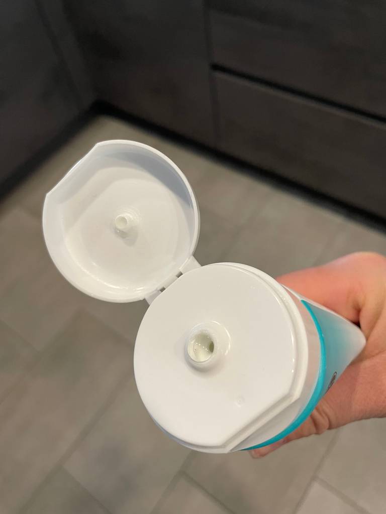Eine Hand hält eine geöffnete Tube getestetes Baby-Shampoo vor einem Badezimmerboden.